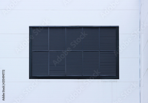 A window in a large industrial shopping center closed with external jalousie in the form of ventilation grilles. light blue background