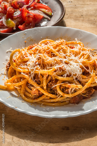 Classical Italian Pasta Amatriciana in a white plate close-up on a rustic wooden table