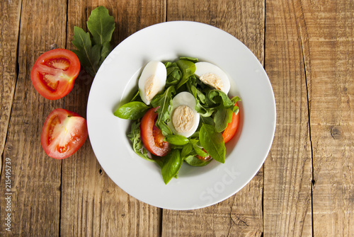 Green health salad with sliced boiled eggs, tomato and fresh lettuce, arugula and spinack served on wooden table. Top view.