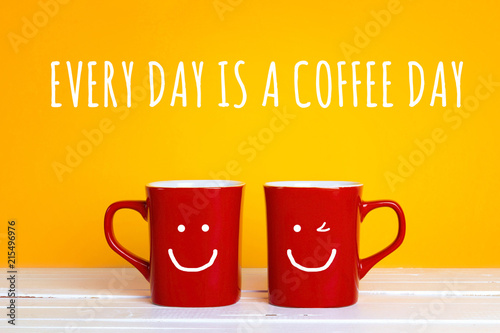Two red coffee mugs with a smiling faces on a yellow background with the phrase Every day is a coffee day.