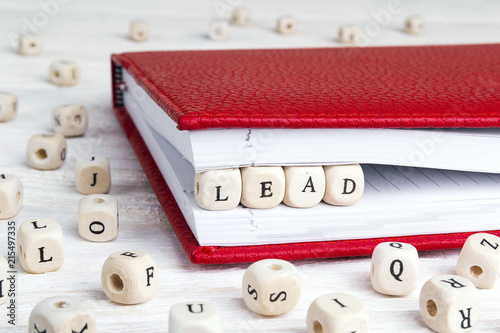 Word Lead written in wooden blocks in red notebook on white wooden table.