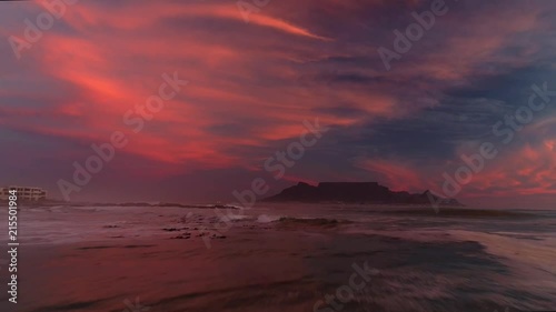 Backwards aerial track and ascend over Bloubergstrand beach with Table Mountain in the background during breathtakingly beautiful and colorful sunset. photo