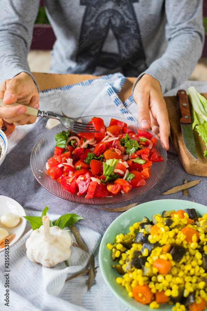 Woman hands holds vegetarian lunch with fresh red tomatoes and salad leaves, cooked vegetables, boiled corn grain, eggplants, carrots. Vegan dinner and healthy food