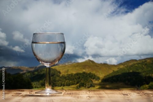 A glass glass glass with clean water stands on a wooden table against a mountain landscape.