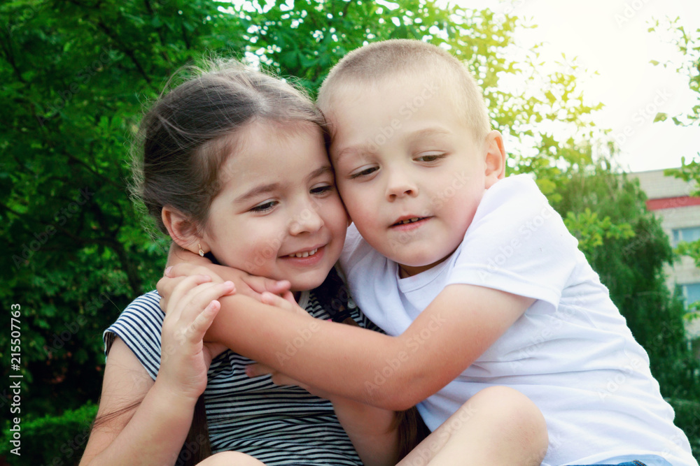 Happy children - boy and girl are sitting on the grass, having fun and embracing. The concept of friendship and family. Happy children - boy and girl are sitting on the grass, having fun and embracing. The concept of friendship and family.