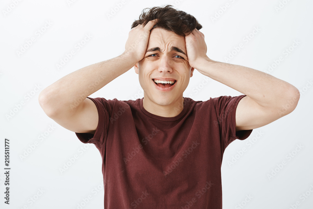 Studio shot of desperate crying caucasian man in red t-shirt, touching hair and screaming or whining, feeling miserable and brokenhearted, standing unhappy over gray background Studio shot of desperate crying caucasian man in red t-shirt, touching hair and screaming or whining, feeling miserable and brokenhearted, standing unhappy over gray background