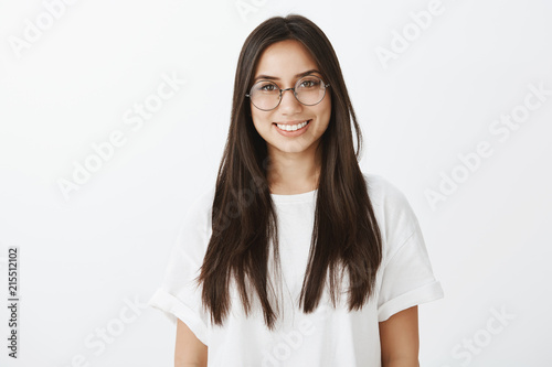 Waist-up shot of carefree confident attractive woman in eyewear and white t-shirt, smiling broadly and gazing at camera with pleased self-assured expression, talking politely with customer photo