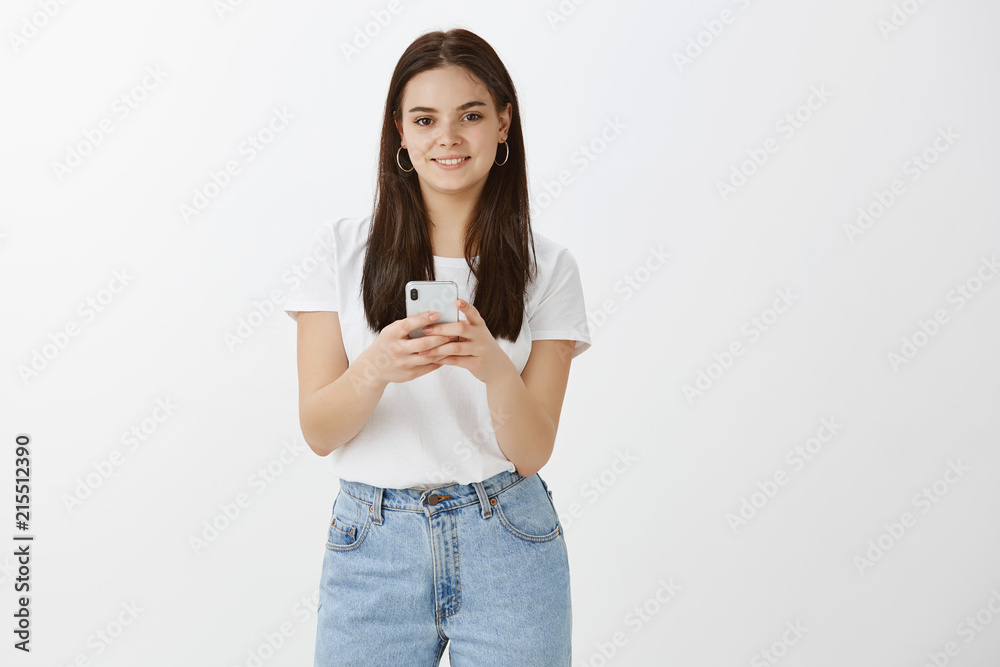 What is your profile nickname again. Stylish modern woman in trendy clothes, holding smartphone and gazing with happy expression at camera, waiting to take picture on phone, standing over grey wall What is your profile nickname again. Stylish modern woman in trendy clothes, holding smartphone and gazing with happy expression at camera, waiting to take picture on phone, standing over grey wall