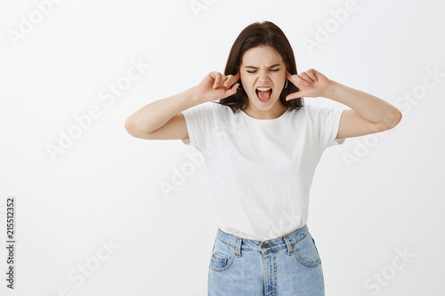 Displeased stressed attractive and stubborn girlfriend in jeans and t-shirt, covering ears with index fingers, shouting or yelling, looking down, arguing and wanting not hear scream of boyfriend