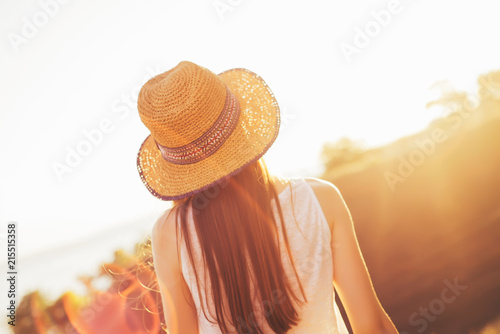A girl in a hat looks at the sunset. Warm summer evening.