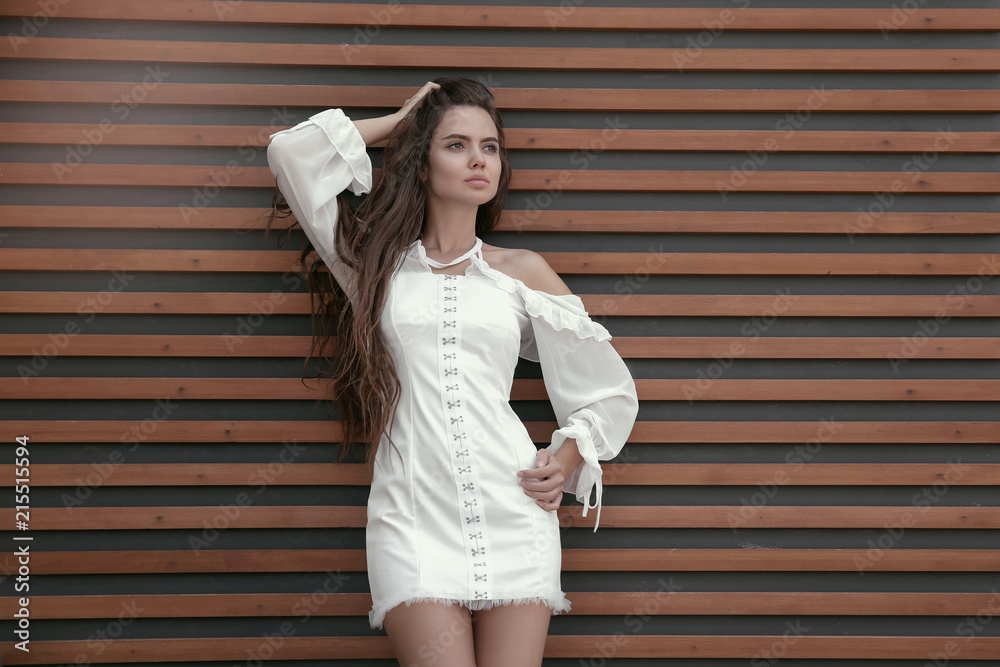 Sexy young brunette girl in white short dress against wooden strip wall,  fashion style outdoor shot. foto de Stock | Adobe Stock