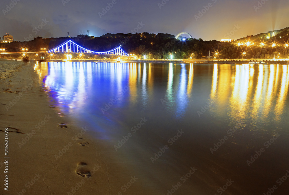 Reflection of the lights of night town and traces on the sand of the embankment