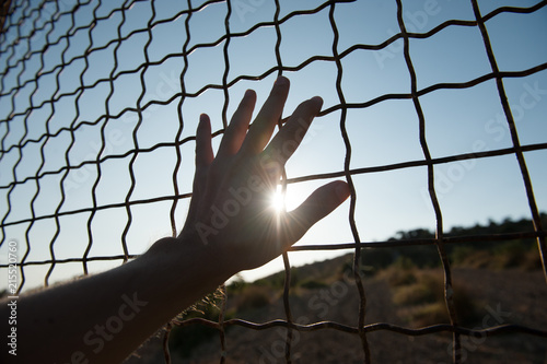 human hand touching fence cage in jail and illegal immigration on sunset