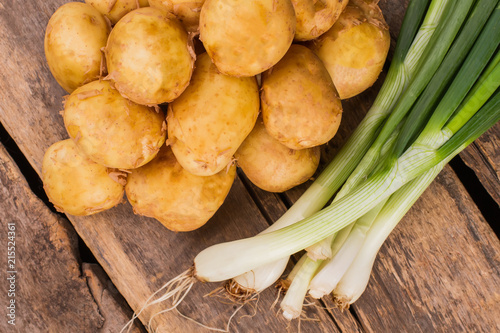 Pile of potatoes and green onion. Top view. Rustic wooden desk background. photo