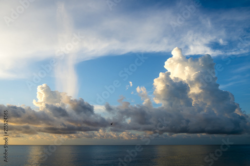 Calm sea with puffy tropical clouds on the horizon at sunrise
