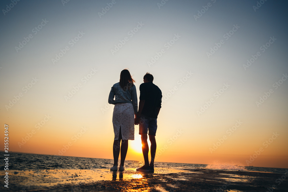 Silhouette of couple standing at the pier, watching the sunrise at the beach summer time