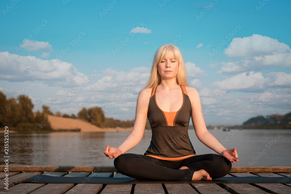 a woman practicing yoga. healthy lifestyle. yoga on the river pier. healthy lifestyle. a woman with blond hair meditates on the background of the river and the sky. a woman practicing yoga. healthy lifestyle. yoga on the river pier. healthy lifestyle. a woman with blond hair meditates on the background of the river and the sky.