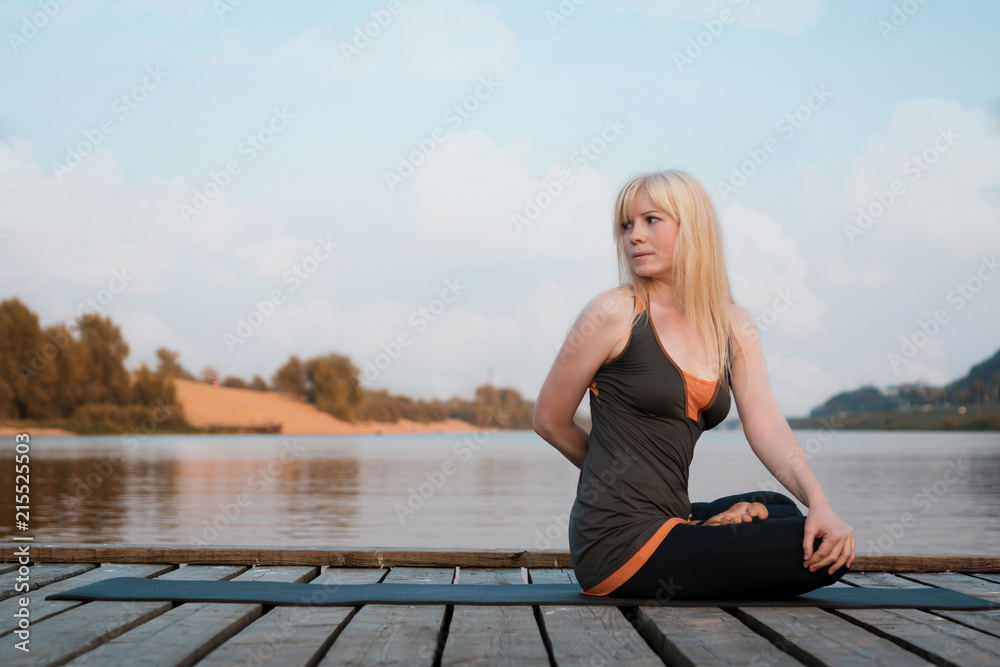 a woman practicing yoga. healthy lifestyle. yoga on the river bridge. against the river, sky and clouds