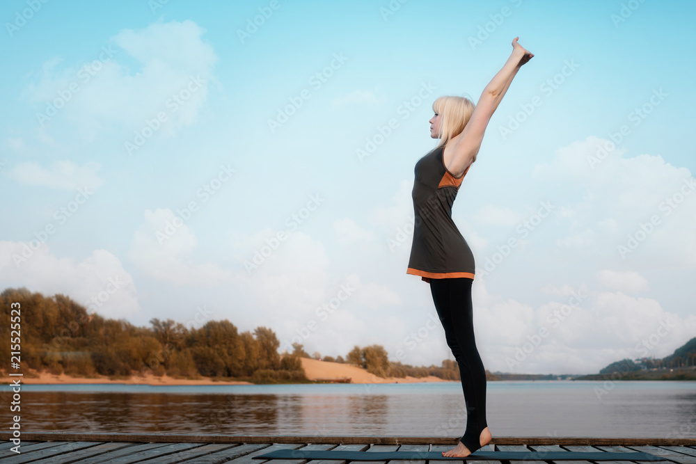 a woman practicing yoga. healthy lifestyle. yoga on the river bridge. against the river, sky and clouds