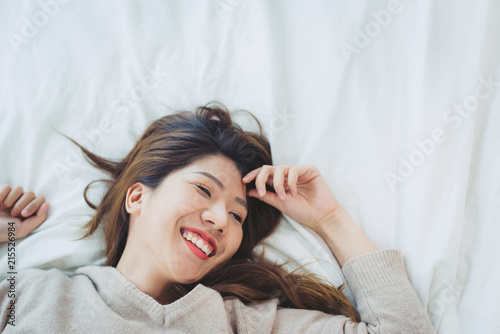 Portrait beautiful young Asian woman on bed at home in the morning. Cheerful Asian woman wearing a comfortable sweater and smiling on her bed. Relaxing room. lifestyle asia woman at home concept.