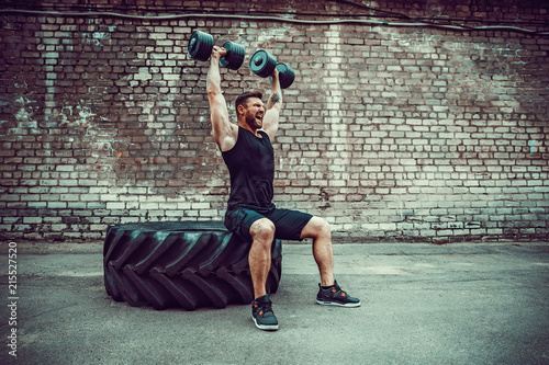 Athletic man working out with a dumbbell in front of brick wall. Strength and motivation. Outdoor workout. Exercise for the shoulder muscles, deltoid.