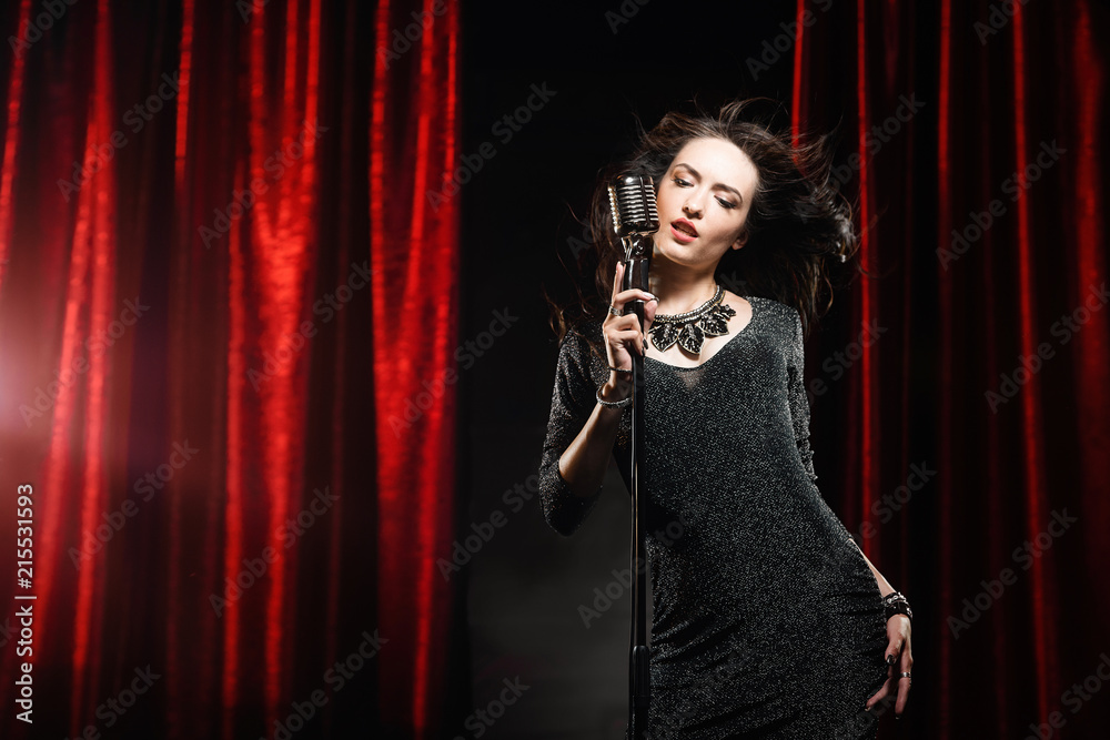 Beautiful girl in black dress singing in the microphone in the concert hall Beautiful girl in black dress singing in the microphone in the concert hall