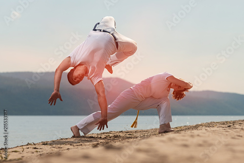 Men train capoeira on the beach - concept about people, lifestyle and sport.