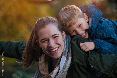 Close-up portrait - laughing positive mom and son playing together while walking in the autumn warm park