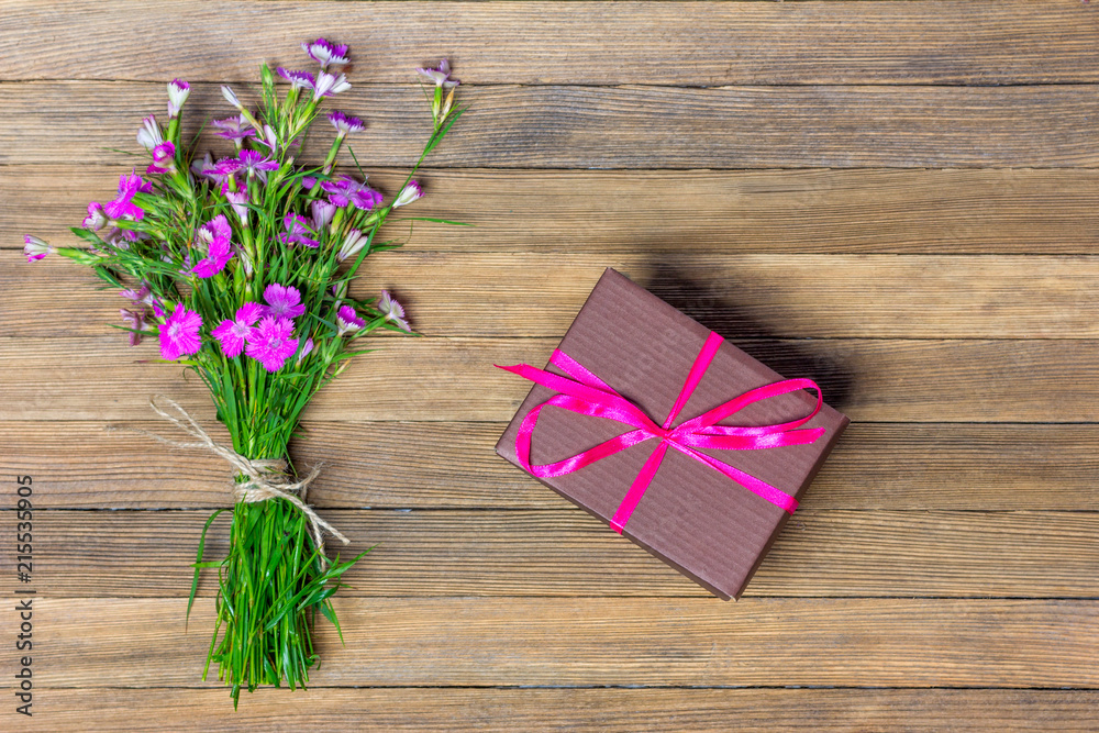 bouquet of carnations and brown box with a gift on a wooden background, flat lay top view