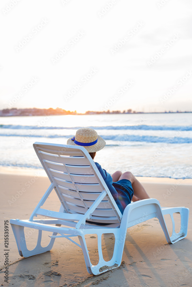 Beautiful girl in a hat sits on a deckchair meeting the dawn. Beautiful girl in a hat sits on a deckchair meeting the dawn.