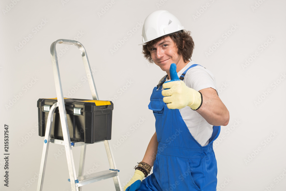 Portrait of handsome builder in white helmet and blue overall showing thumbs up and laughing. Portrait of handsome builder in white helmet and blue overall showing thumbs up and laughing.