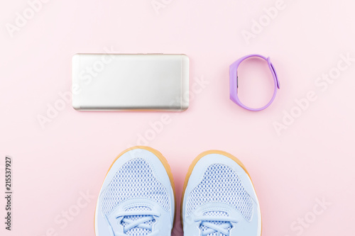 Woman sneakers, fitness tracker and smartphone on pastel pink background. Sport fashion concept. Flat lay