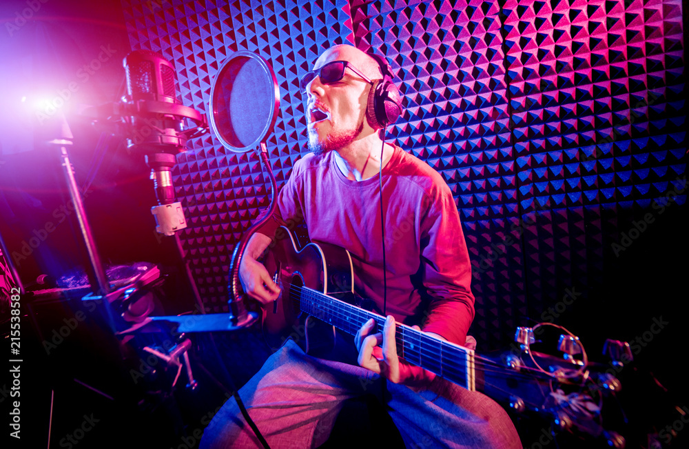 Obraz premium The singer sings with a microphone and playing guitar in the recording studio.