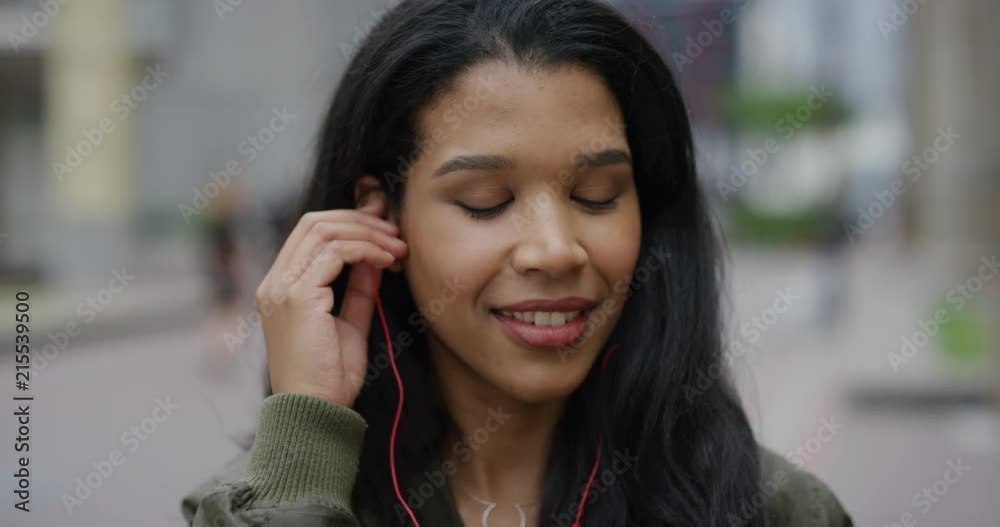close up happy young mixed race woman laughing takes off earphones enjoying relaxed urban lifestyle listening to music on city street close up happy young mixed race woman laughing takes off earphones enjoying relaxed urban lifestyle listening to music on city street