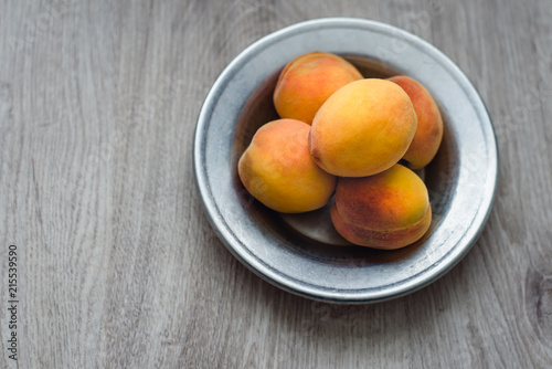 Still life of peaches in a rustic plate on a wooden background