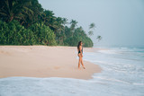 The concept of travel, tourism, recreation at sea, people. A young girl in a bikini strolls along the shore of a pink beach, the waves tenderly touch her feet.