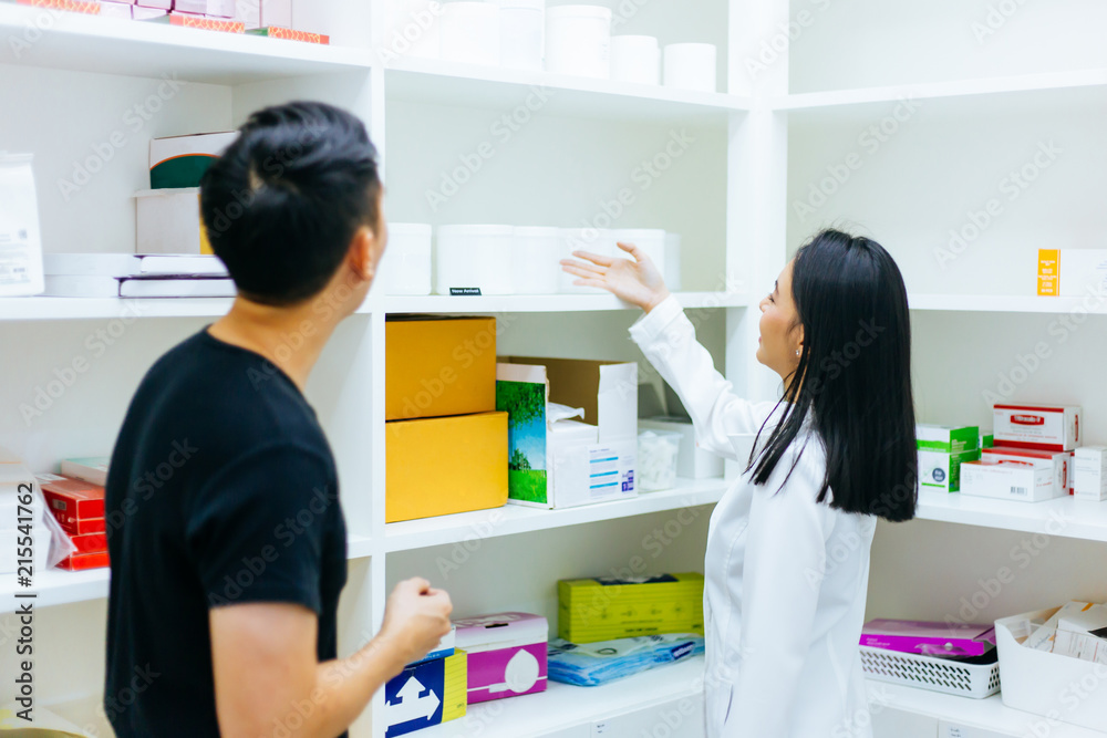 Asian female pharmacist doctor in professional gown explaining and giving advice with male client in drugstore shop.