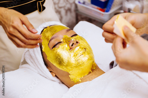 Beauty clinic staff helping young woman getting 24 karat gold facial treatment at the beauty clinic. The treatment of using real gold for youthful skin. photo