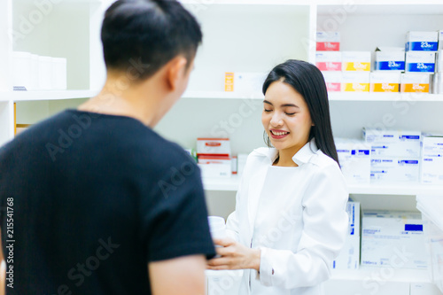 Asian female pharmacist doctor in professional gown explaining and giving advice with male client in drugstore shop.