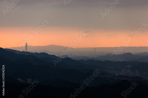 Taipei Taiwan city silhouette, sunset colors with outline of Taipei 101 building visible, orange color horizon in background and layered silhouettes of the mountains surrounding the city.