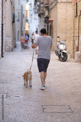 A man with a dog on a leash on a narrow street of an ancient city. Bari, Italy
