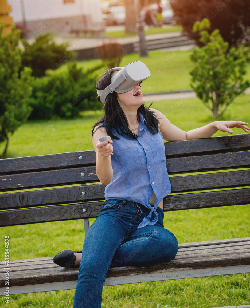 A beautiful young girl plays a game wearing virtual reality glasses on the street. A beautiful young girl plays a game wearing virtual reality glasses on the street.