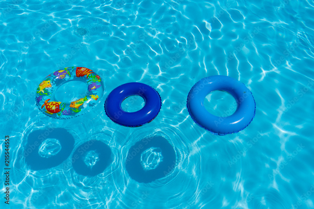Top view of three inflatable buoys floating on a blue swimming pool water. Holidays and summer concept.