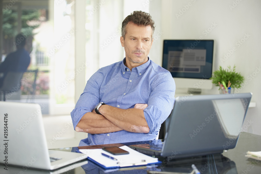 Businessman looking thoughtfully while sitting in front of laptop
