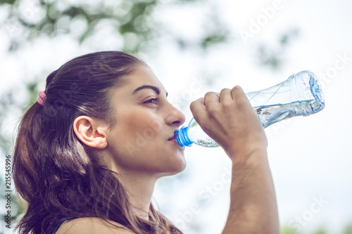 Portrait of beautiful dark-haired girl drinking water at summer green park