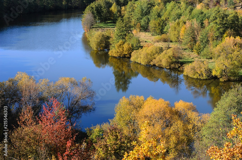 Gorgeous scenic view from above of wide river with autumn yellow, green and red trees on its banks