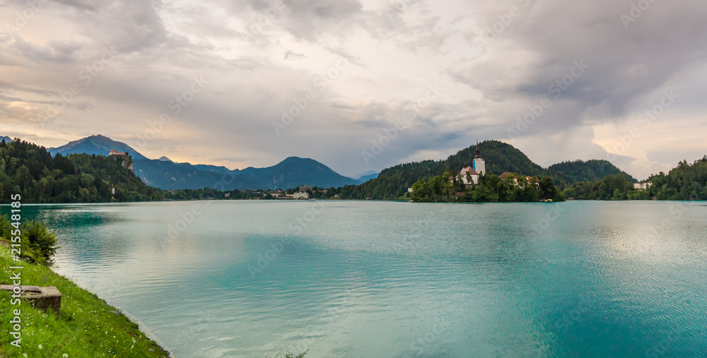 Bled lake with the island and church. Blue water and storm clouds.