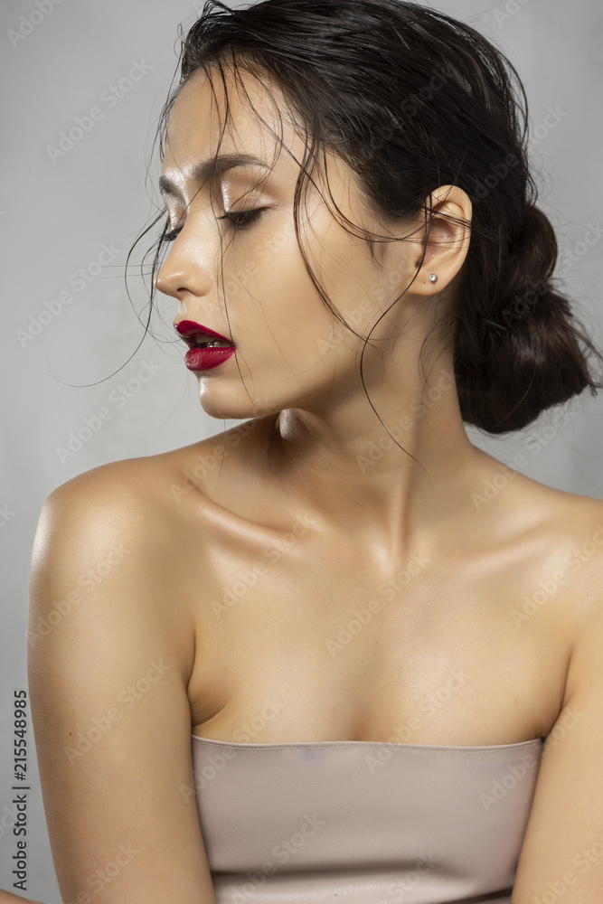 Beautiful brunette girl fashion model with naked shoulders and wet hair on a gray background. Nude make-up, red lips. Healthy clean skin