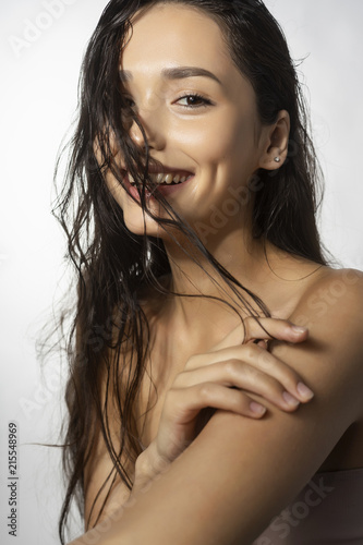 Beautiful smiling brunette girl fashion model with naked shoulders and wet hair on a white background. Nude make-up. Healthy clean skin.