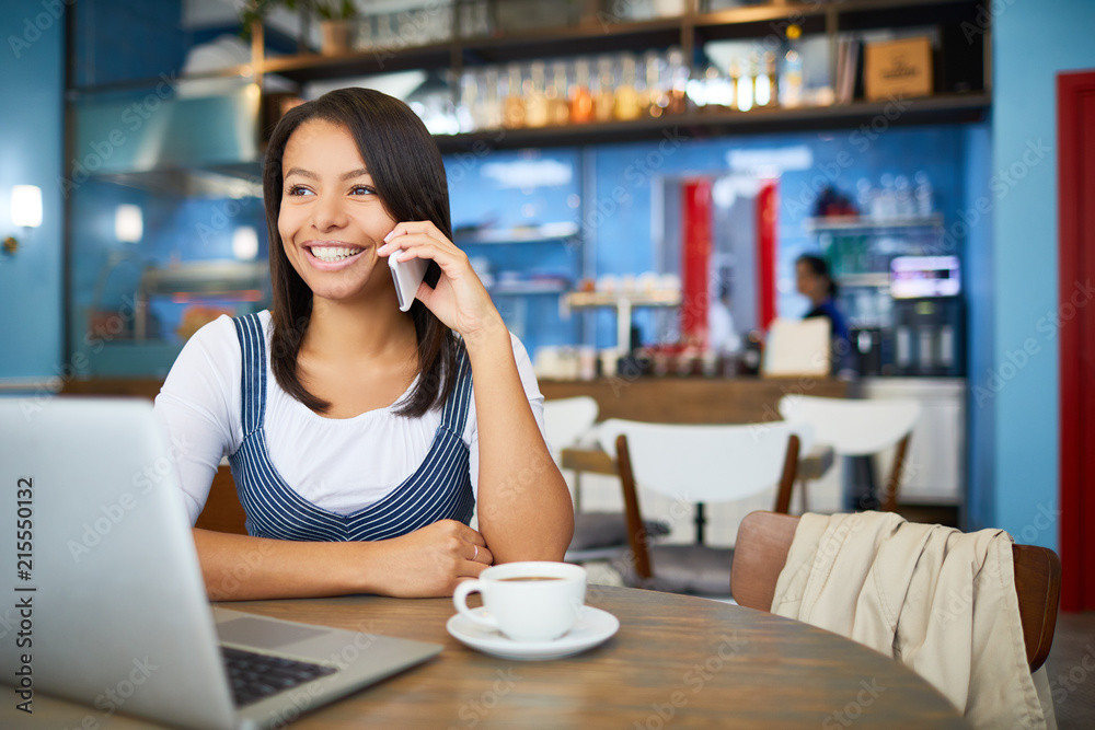 Smiling businesswoman in casualwear sitting by table in cafe, having drink and phoning to someone Smiling businesswoman in casualwear sitting by table in cafe, having drink and phoning to someone